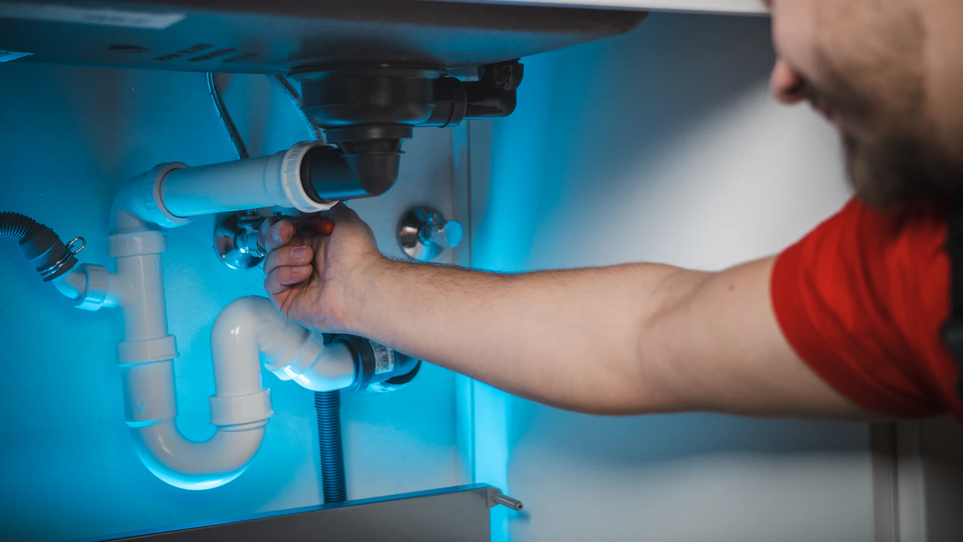 A plumber working on pipes inside a residential wall.