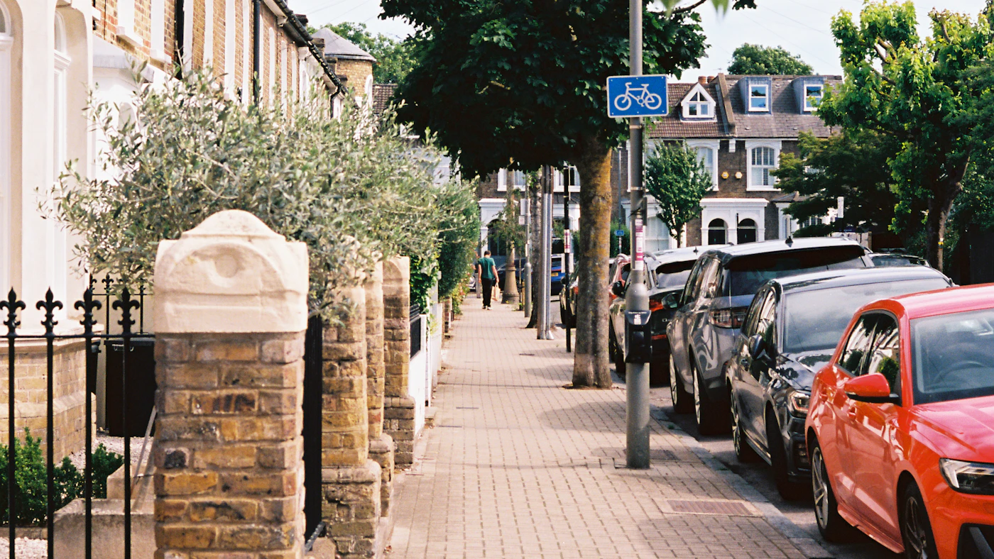 A residential street lined with houses and parked cars.