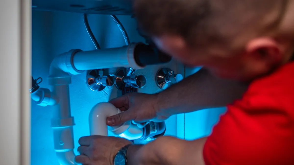 Plumber repairing a pipe beneath a cabinet